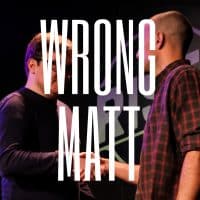 Two men shake hands on a dark stage, partly obscured by large white text reading WRONG MATT. One man wears glasses and a dark sweater, the other a plaid shirt.