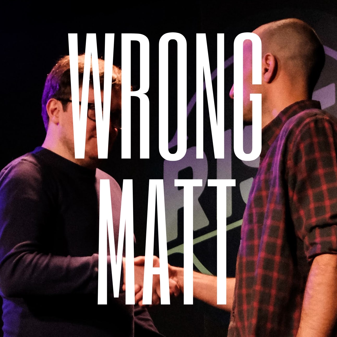 Two men shake hands on a dark stage, partly obscured by large white text reading WRONG MATT. One man wears glasses and a dark sweater, the other a plaid shirt.