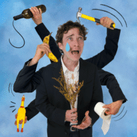 A man in a suit with multiple arms looks distressed, holding a bottle, hammer, banana, rubber chicken, toilet paper, and dried flowers. A cartoon tear is drawn on his face, and the background is light blue.