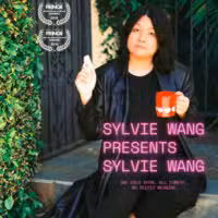 A person with long dark hair in a black coat sits on outdoor steps, holding a red mug and a cigarette. Text reads SYLVIE WANG PRESENTS SYLVIE WANG and two award symbols appear in the top left corner.